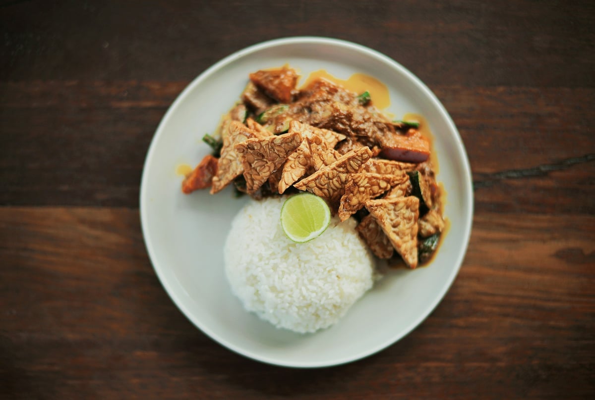 A plate of rice with fried tempeh and lime