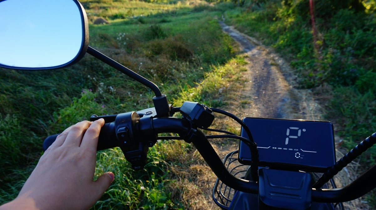 A rider's hand on a scooter's handlebar on a rural path