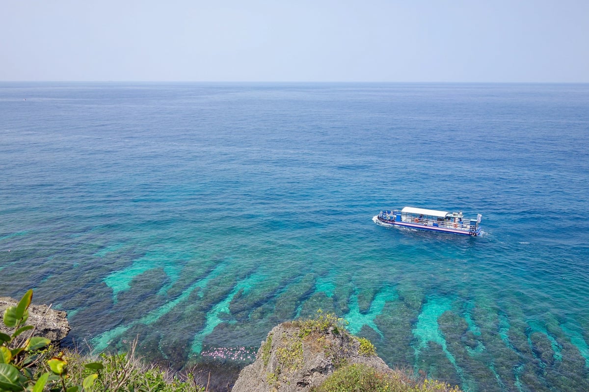 A boat over a coral reef seen from a clifftop