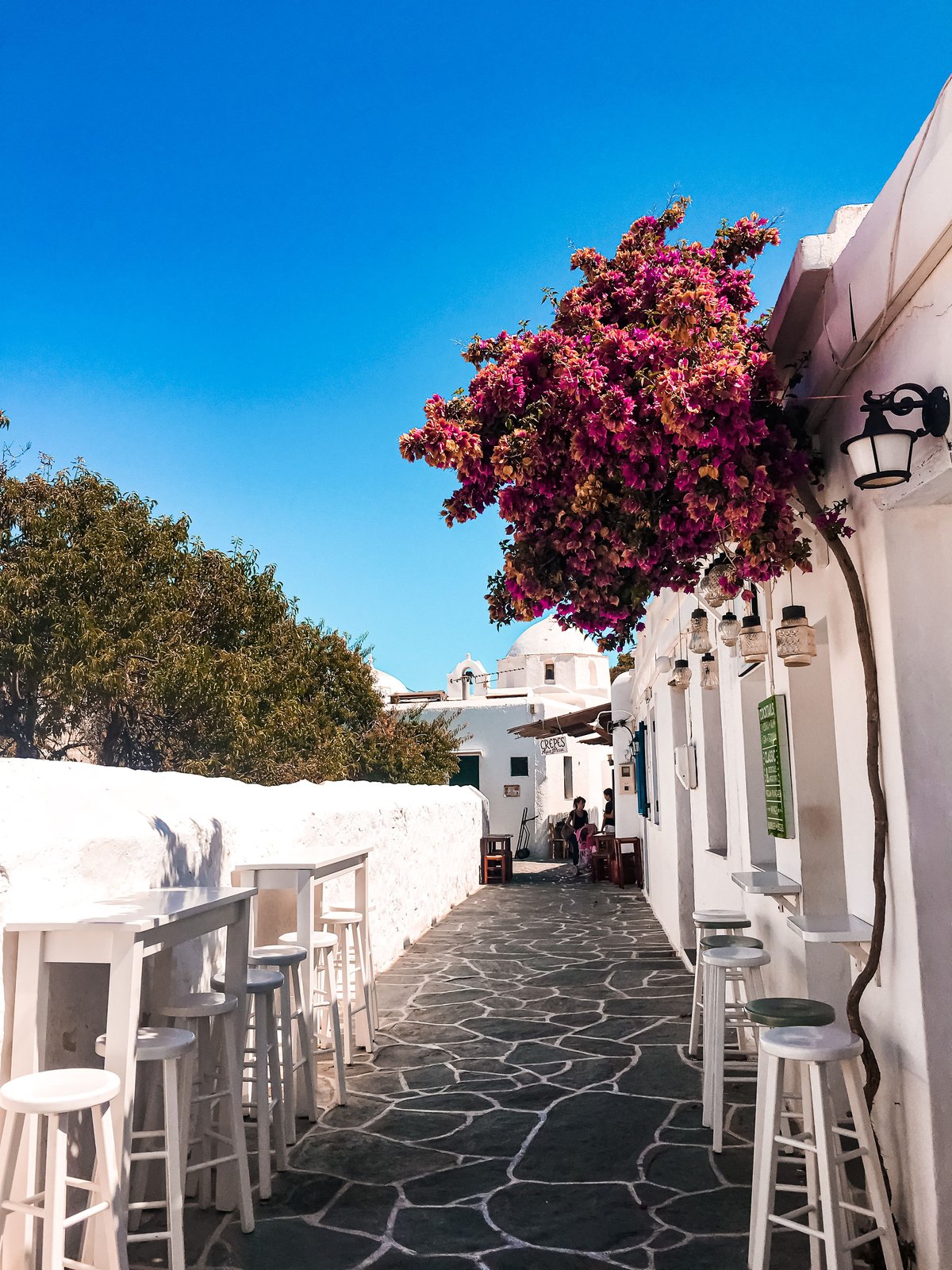 People relaxing at outdoor café tables in a sunny Greek square