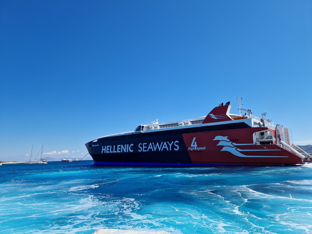 A Greek ferry pulling into a Cycladic port, deck passengers watching whitewashed town