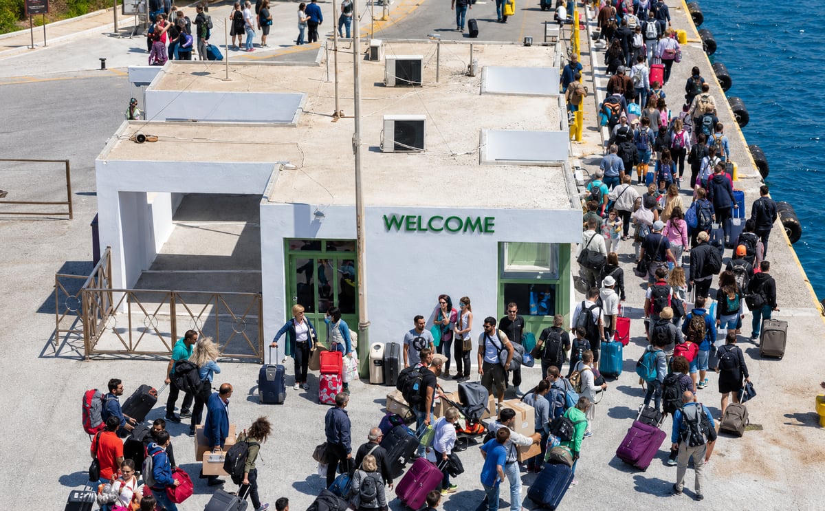 Travelers with luggage waiting at a busy Cycladic ferry port