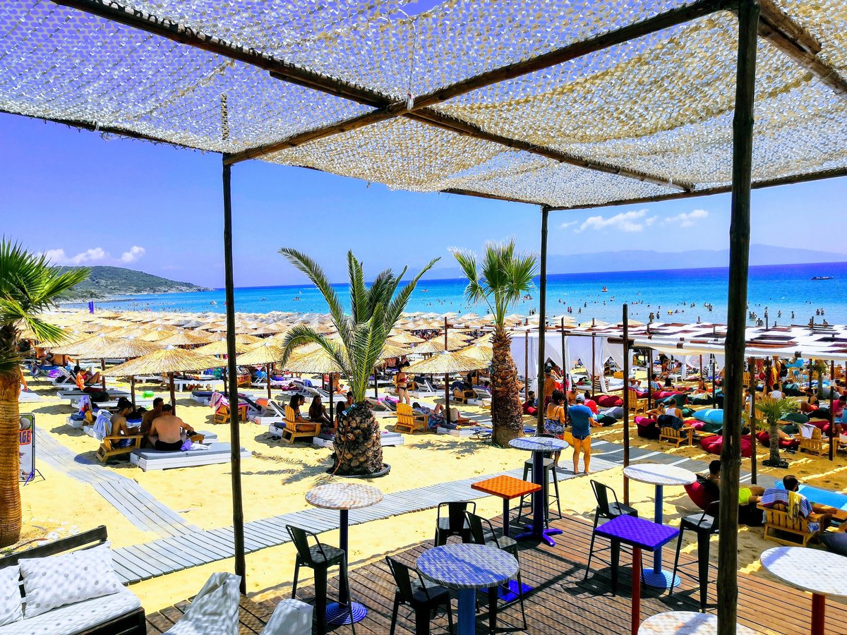 A lively Mykonos beach club scene with loungers and a bar, daytime