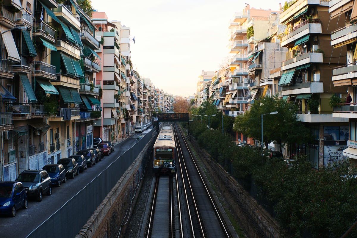 An Athens metro train running through an open track cutting between apartment blocks in daylight