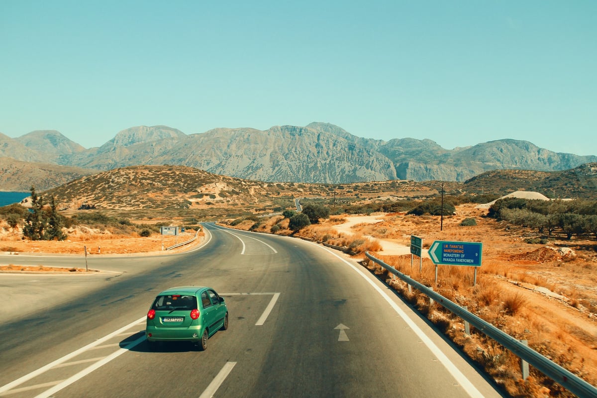 A small rental car parked at a scenic Greek viewpoint or village