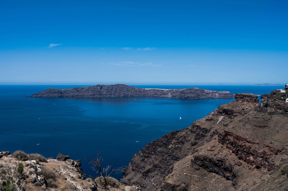 A Mykonos beach club or Little Venice scene contrasted with a calm Santorini caldera view