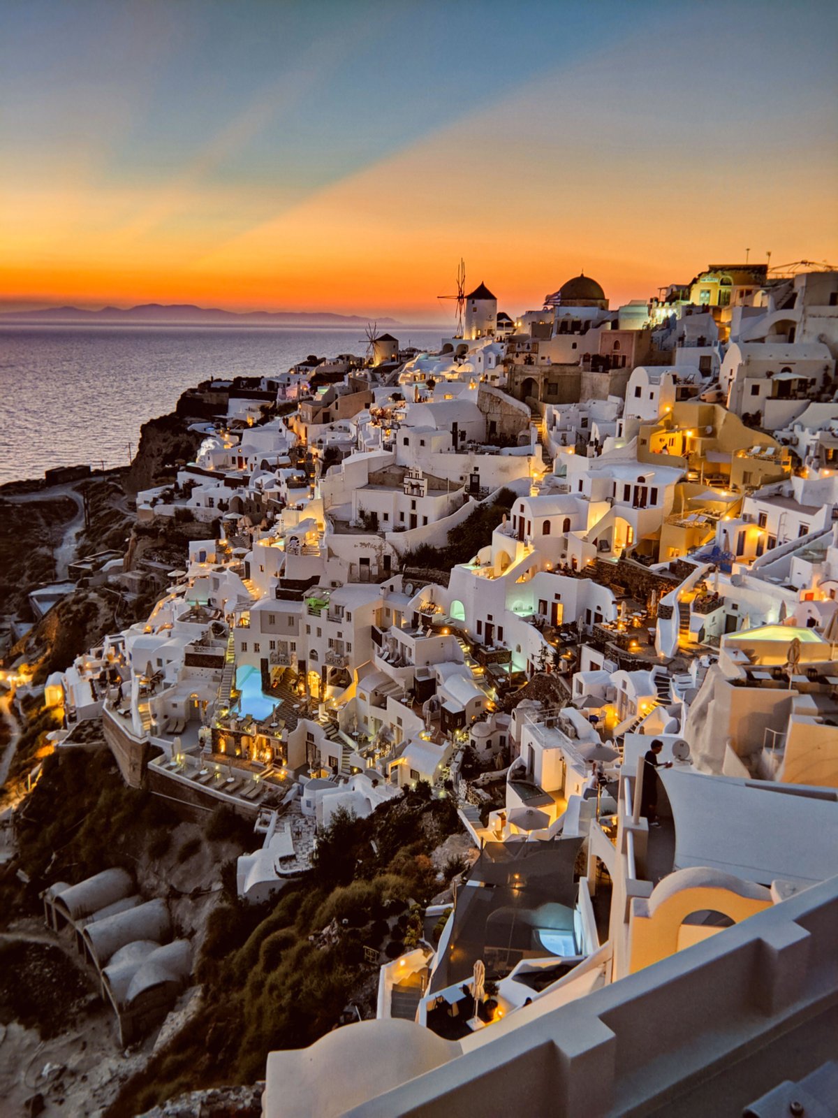 Caldera-edge hotels in Oia at golden hour, infinity pools above the sea