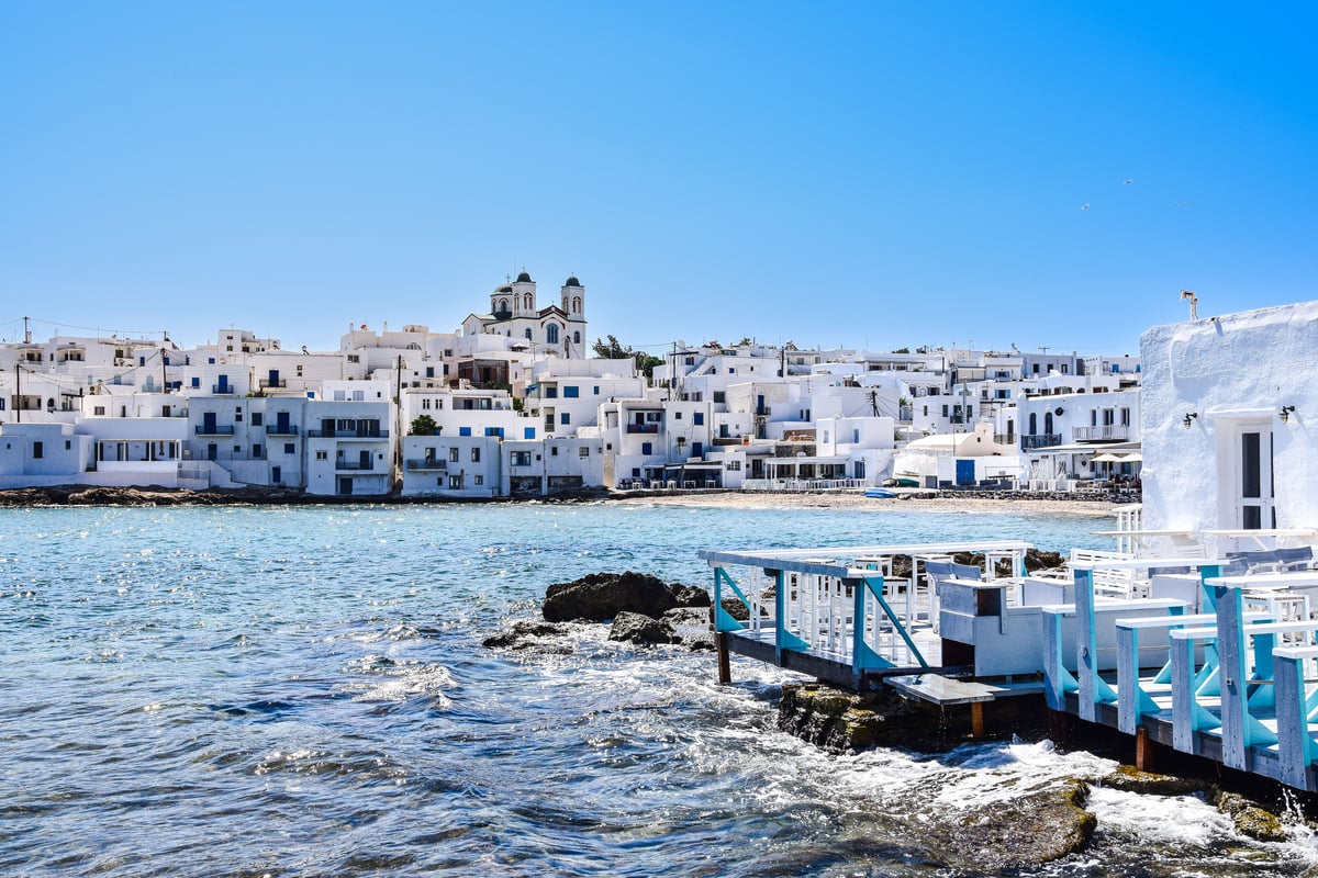 A montage-feel Cycladic scene — white villages, blue domes, turquoise sea