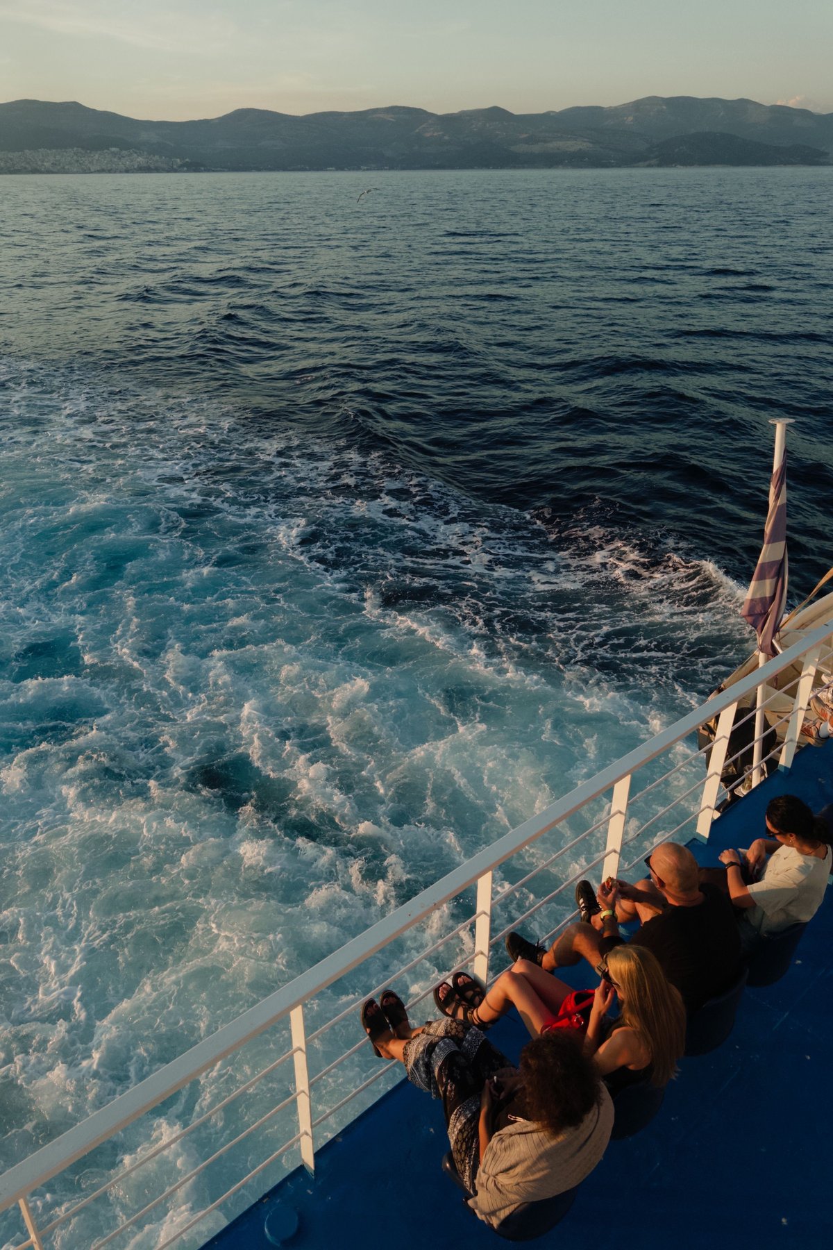 A ferry crossing between two Cycladic islands, blue water and a town on the horizon