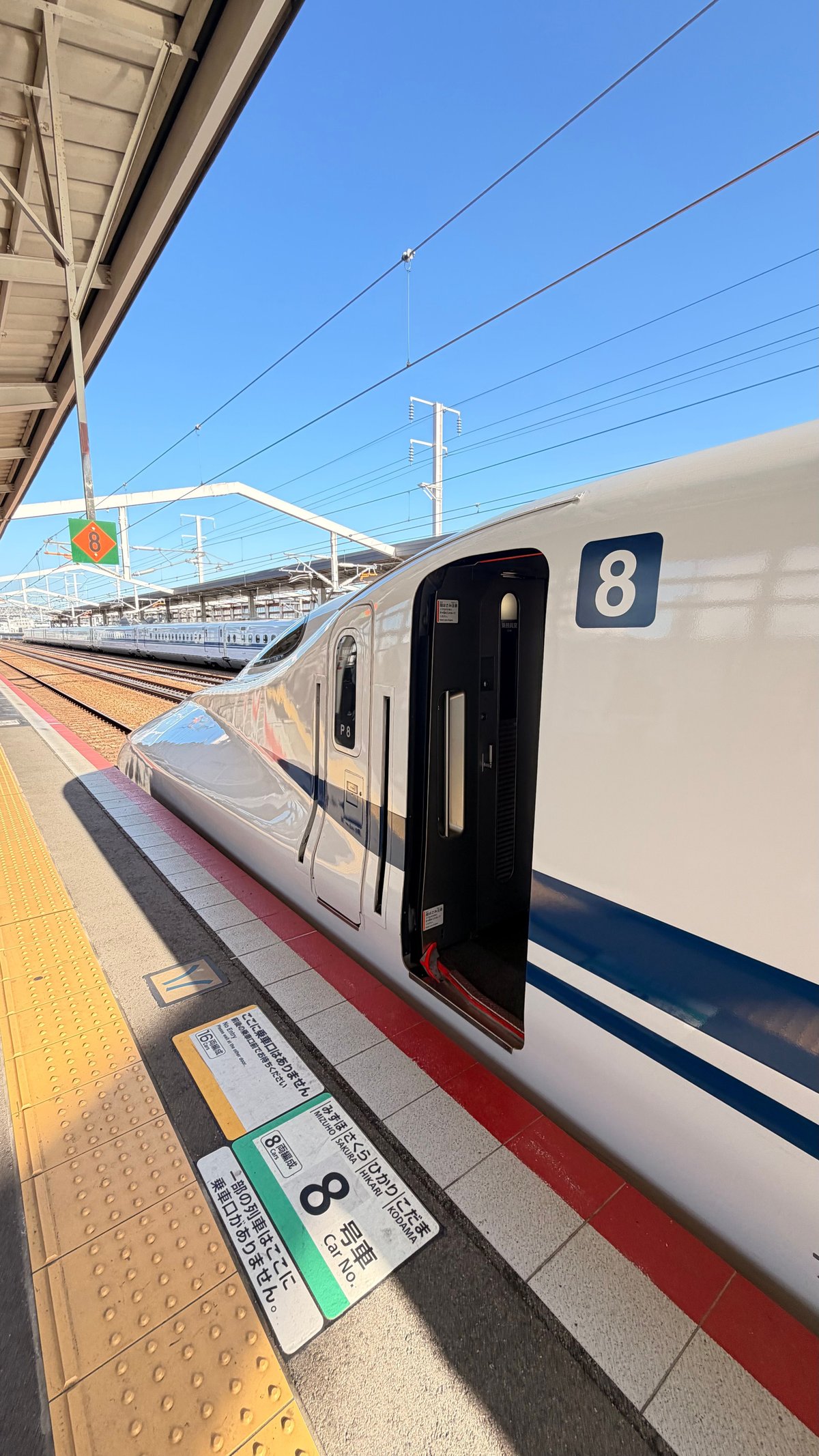 A Shinkansen bullet train at a station platform under a clear blue sky