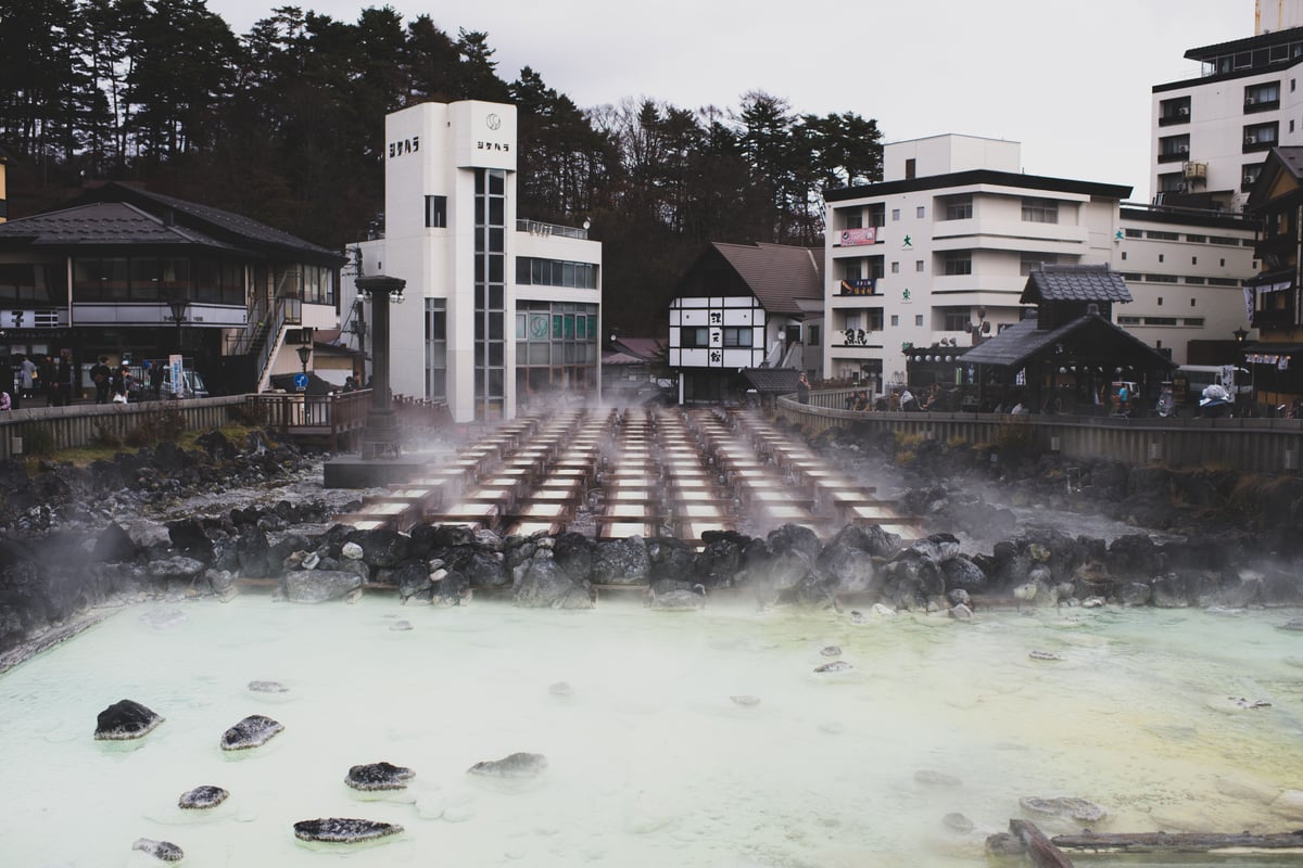 The steaming Yubatake hot water field in an onsen town, wooden cooling channels and traditional buildings