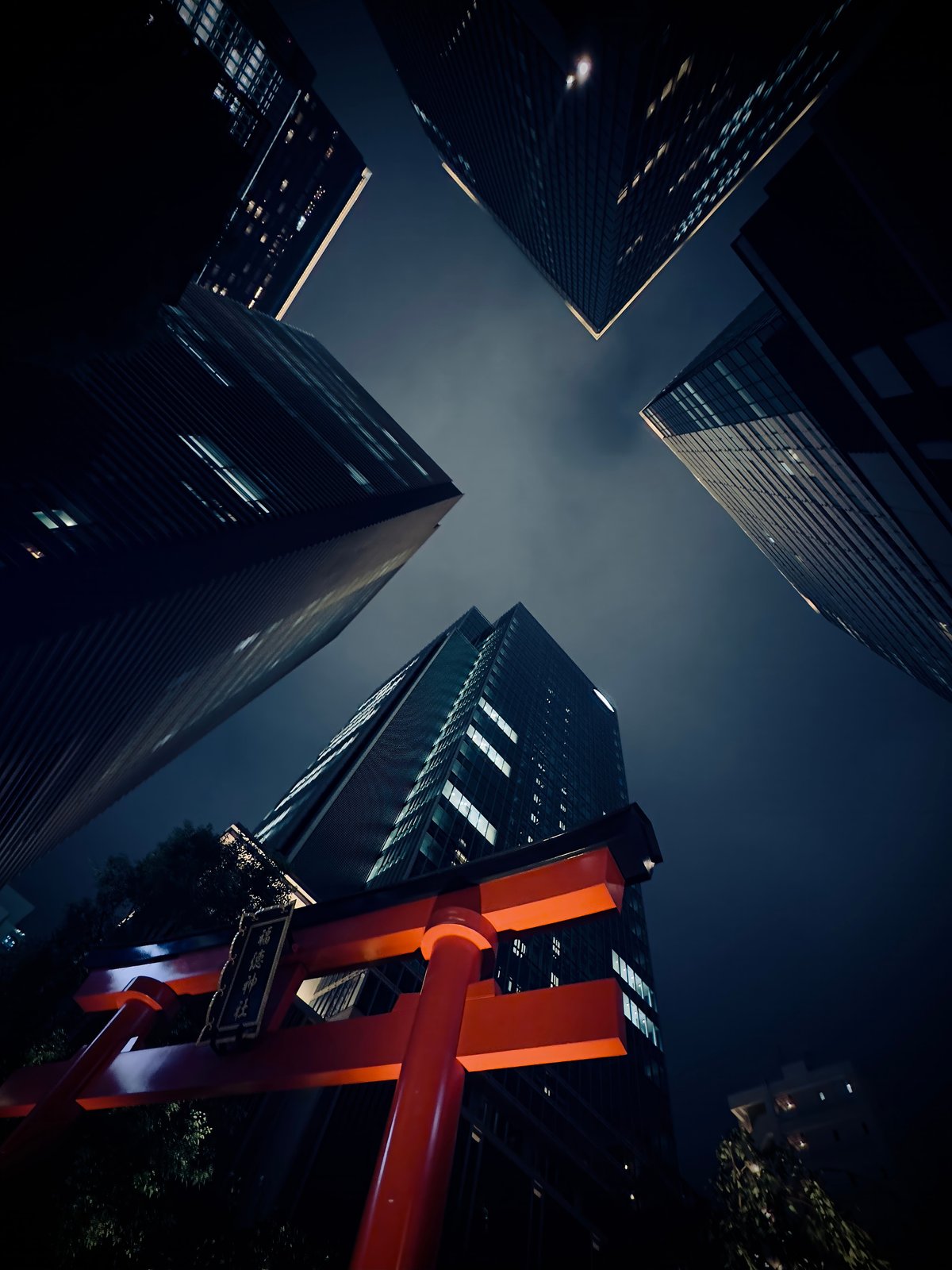 A red torii gate seen from below against Tokyo skyscrapers at night