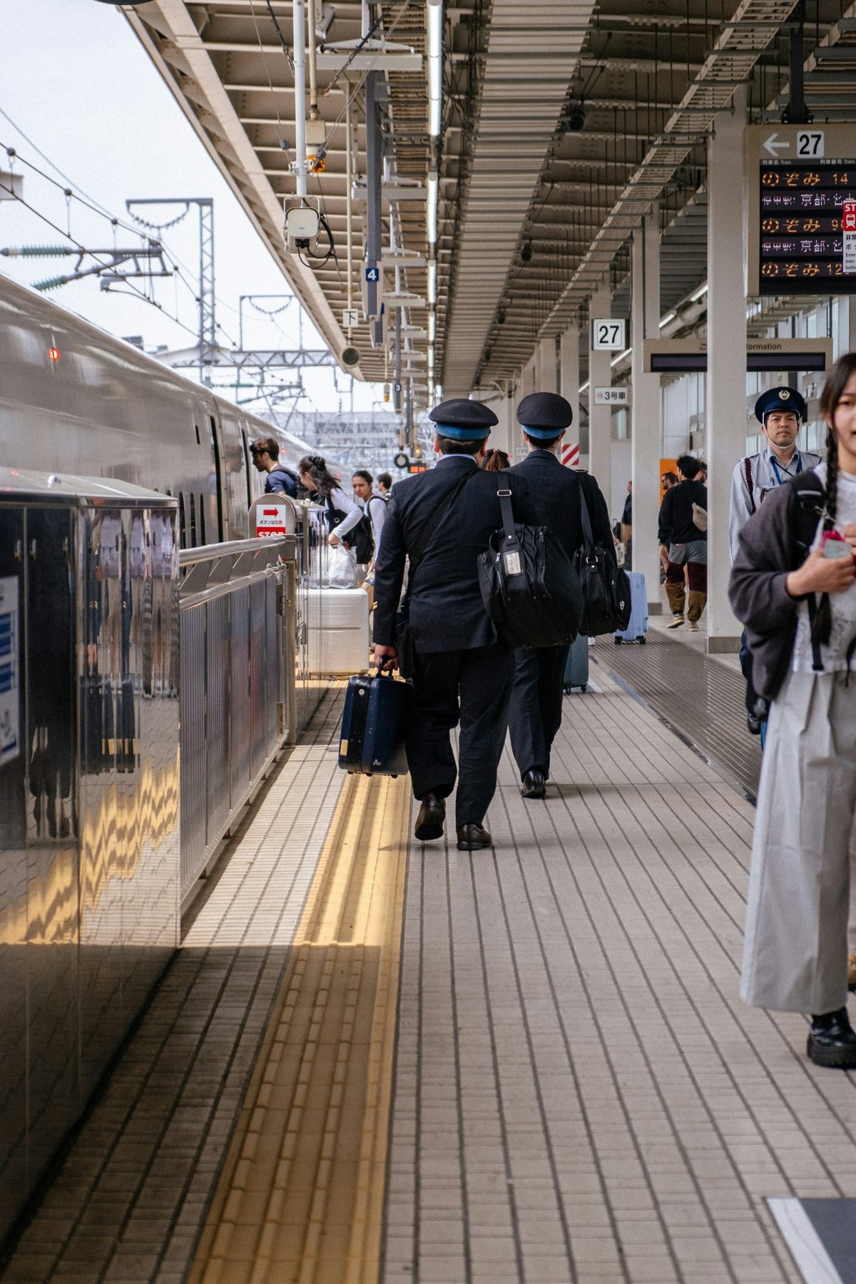 Platform staff and a moderate crowd, backs turned, Shinkansen-style setting