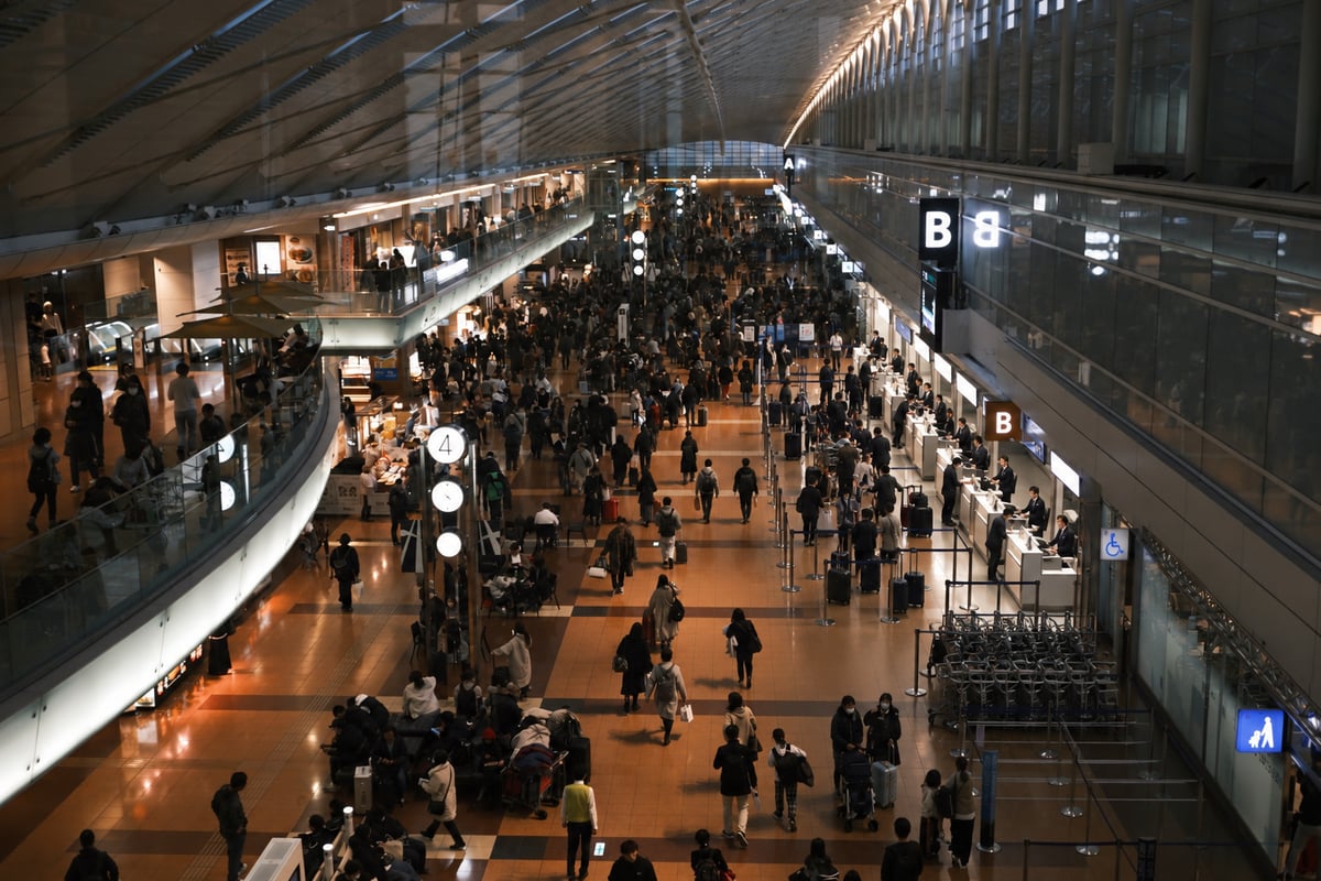 Travelers with suitcases queuing at check-in counters in the international departure hall of a Japanese airport