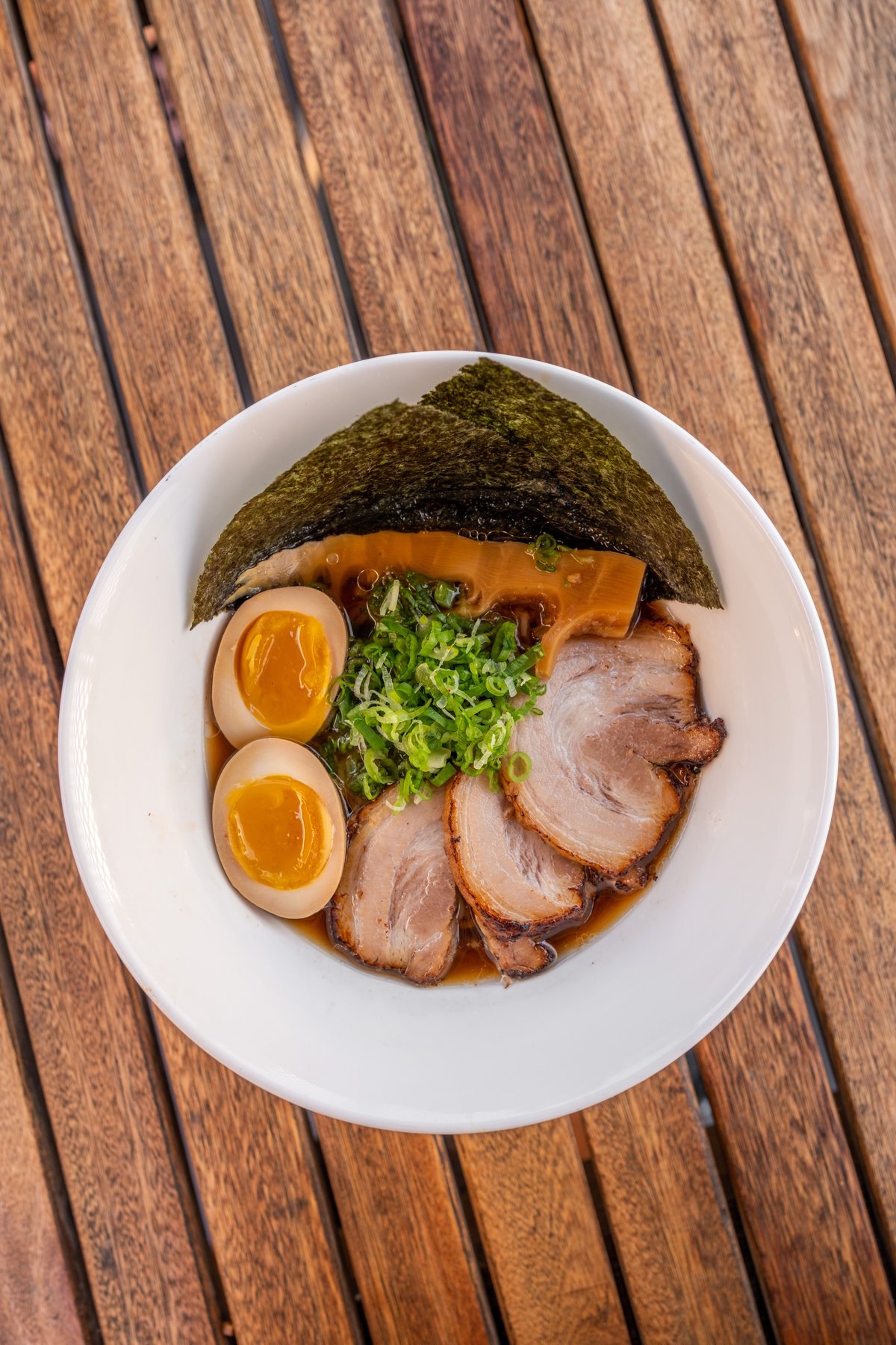 A bowl of ramen with chashu pork, soft-boiled egg, nori, and green onions