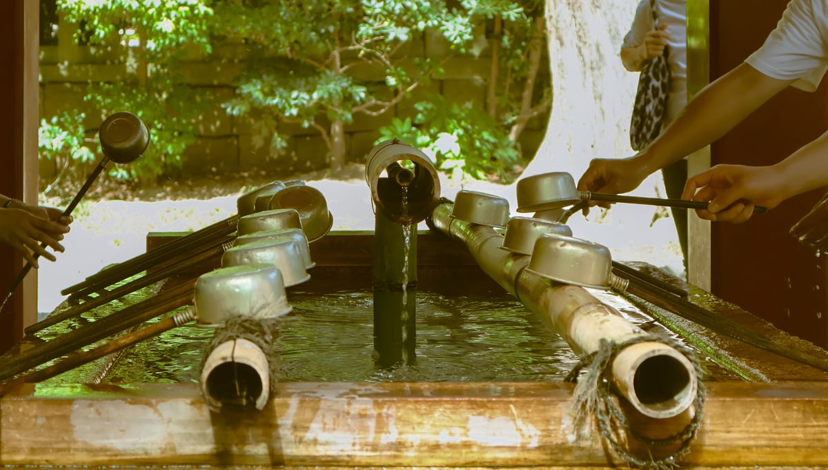 Hands using bamboo ladles at a temizuya water purification basin