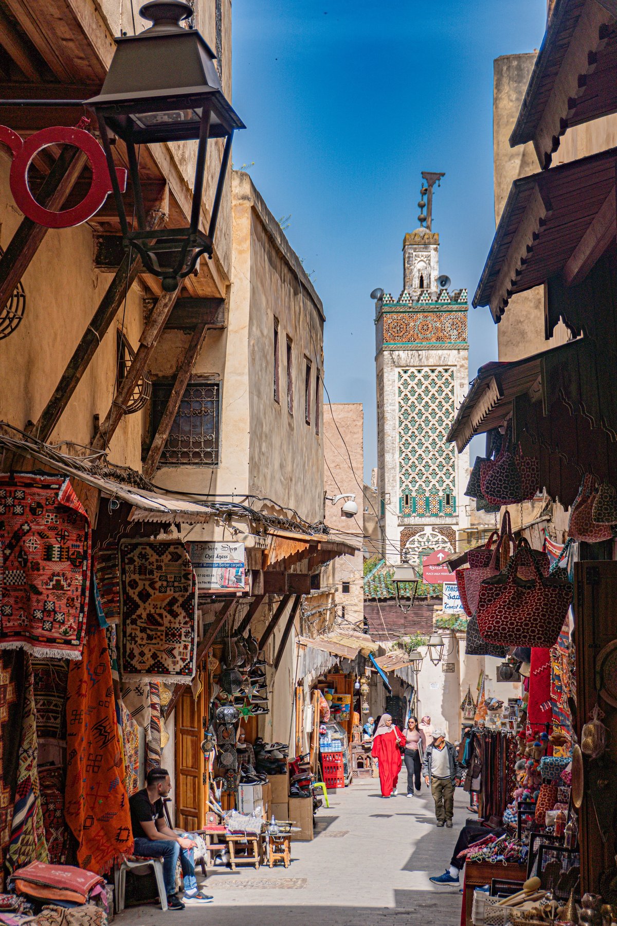 A busy Fez medina lane with shopfronts and figures at a distance, no identifiable faces