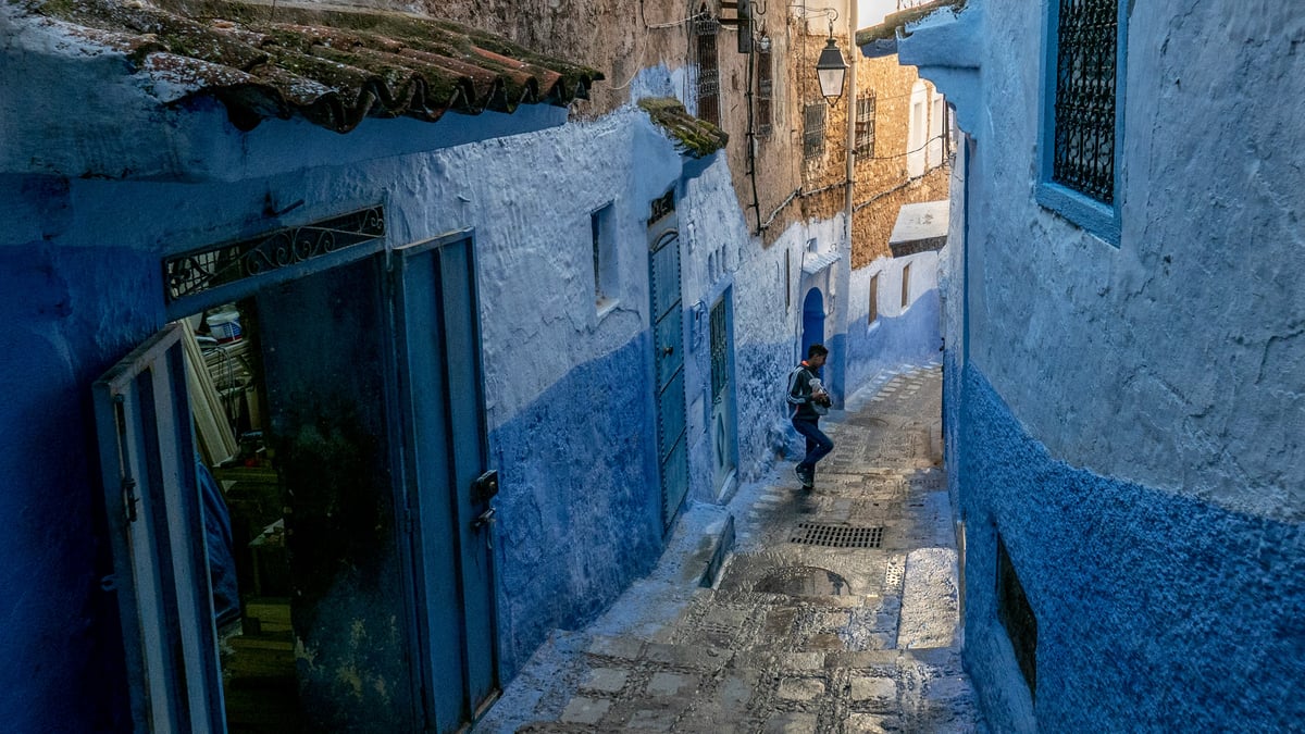 The blue-washed streets of Chefchaouen climbing a hillside, no clear faces