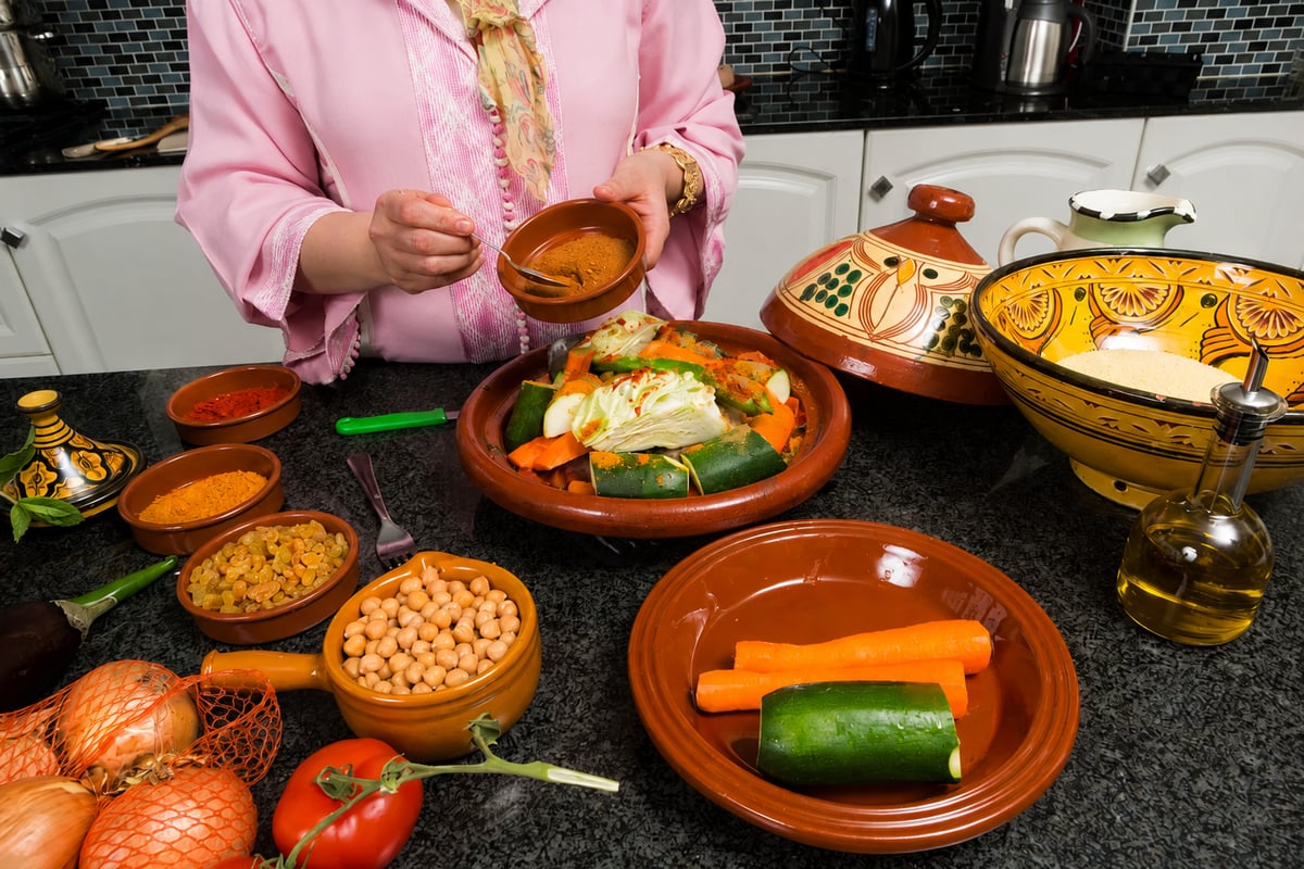 Hands preparing a tagine with fresh vegetables and spices, no faces