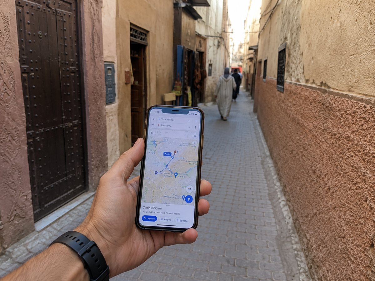 A traveler holding a phone showing a maps app in a narrow medina lane, no faces