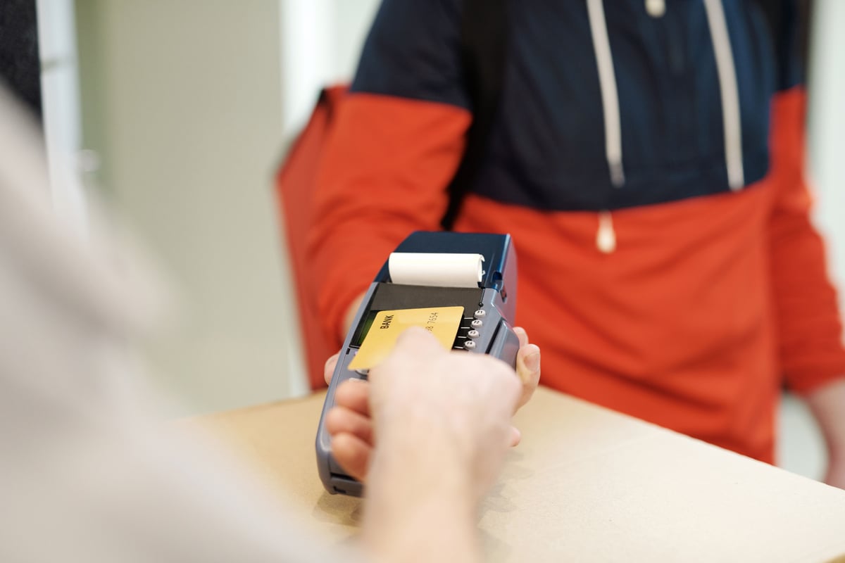 A card payment terminal held by a shopkeeper, screen generic, no faces
