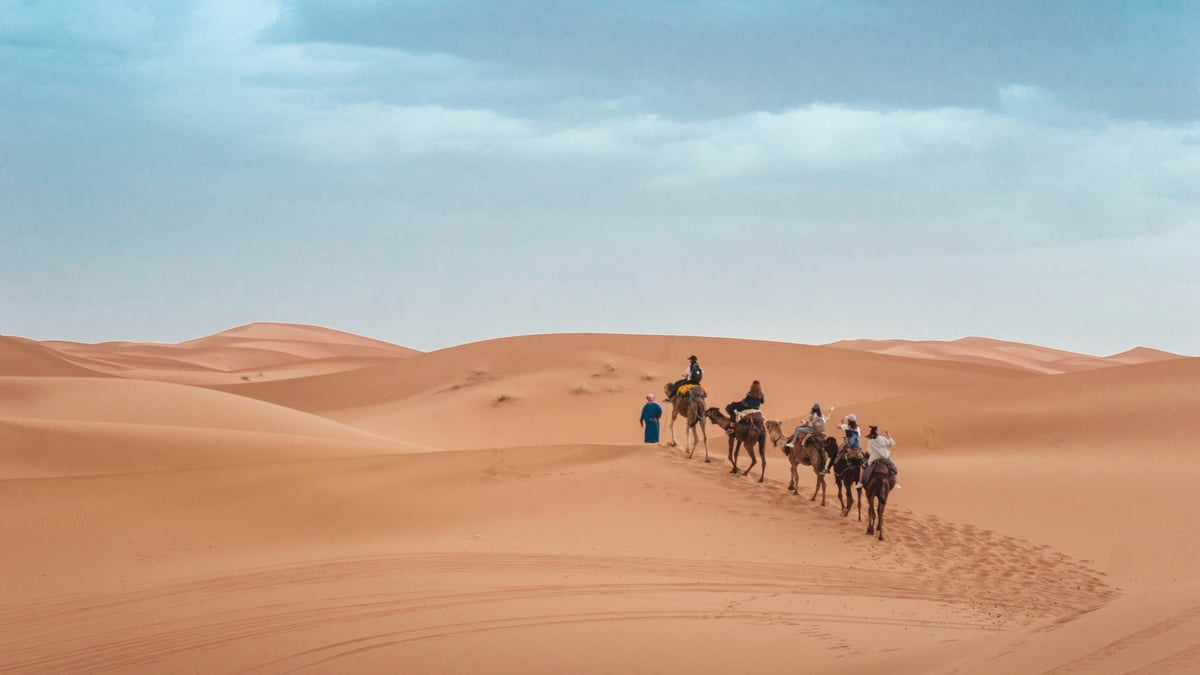 A camel trek in the desert dunes at sunset, no clear faces