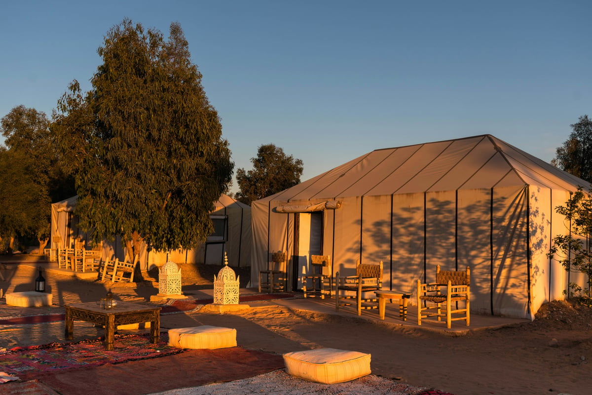 A desert camp at dawn with soft light on the dunes, no clear faces