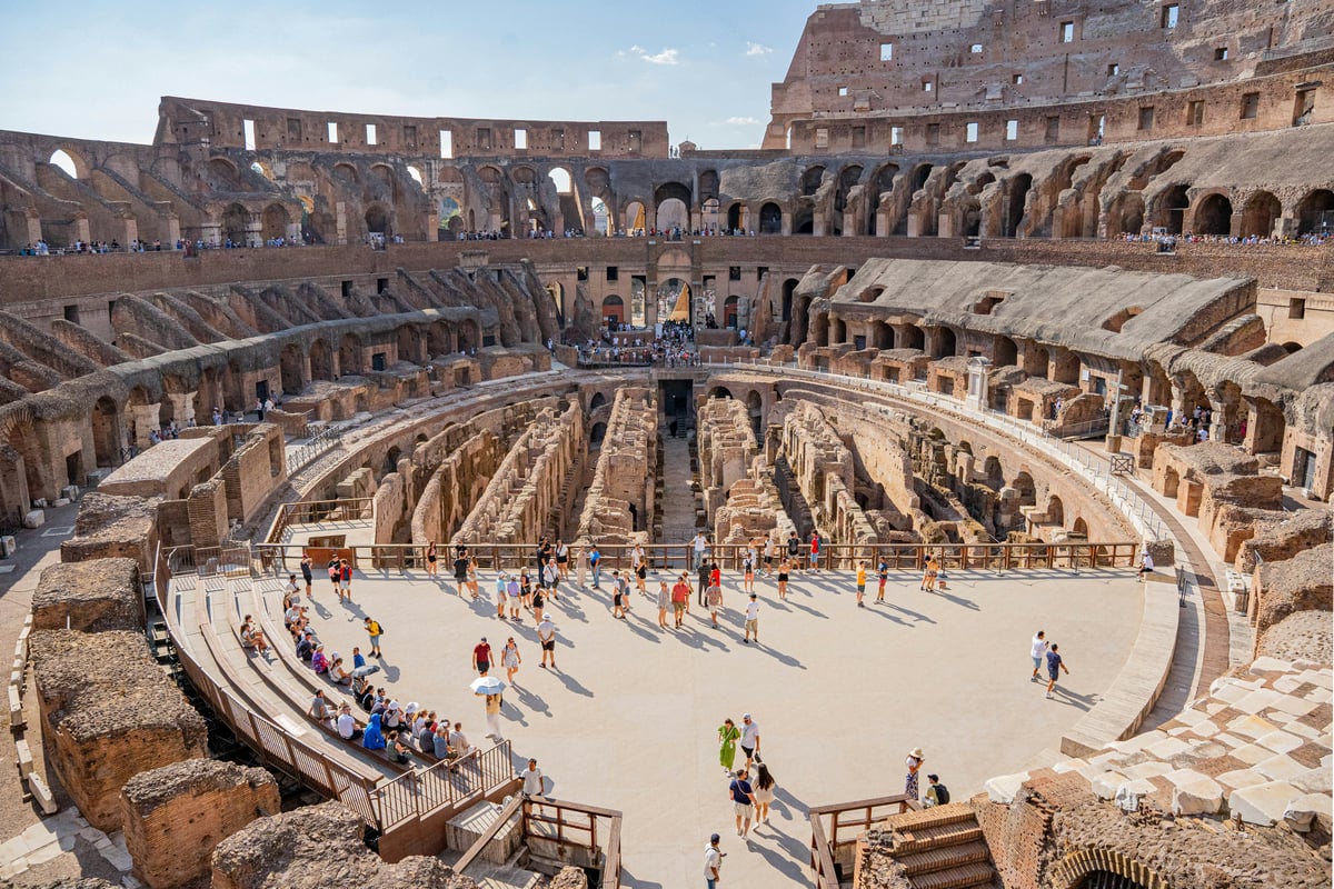 Inside the Colosseum: visitors standing on the reconstructed arena floor, with the excavated underground chambers exposed alongside it