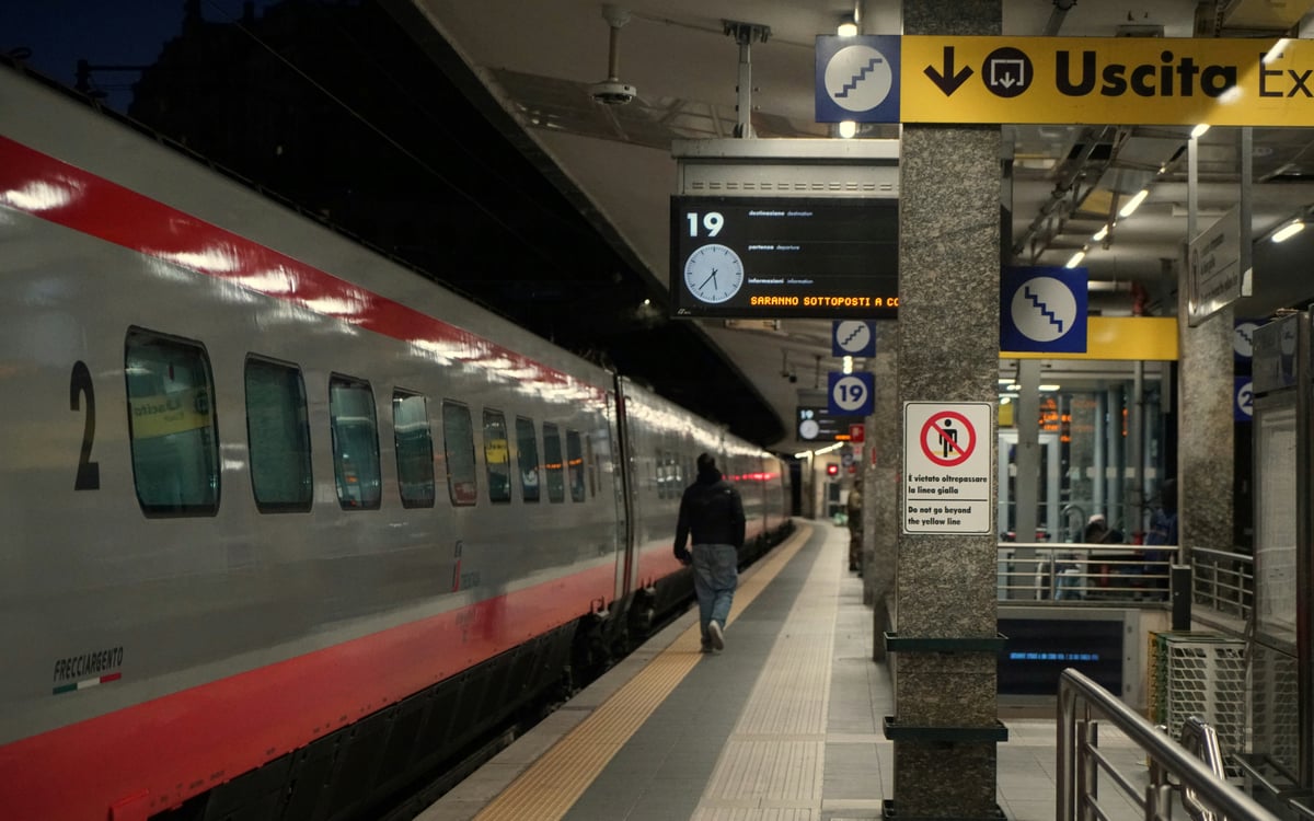 A Trenitalia carriage waiting at an Italian station platform beneath an Uscita exit sign