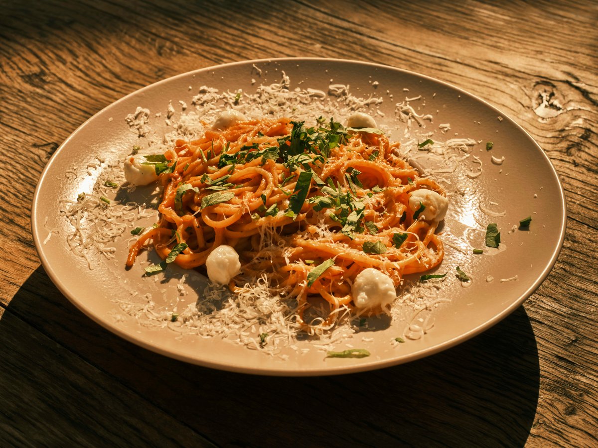 A plate of tomato-sauced spaghetti under a heavy dusting of grated hard cheese, on a rustic table