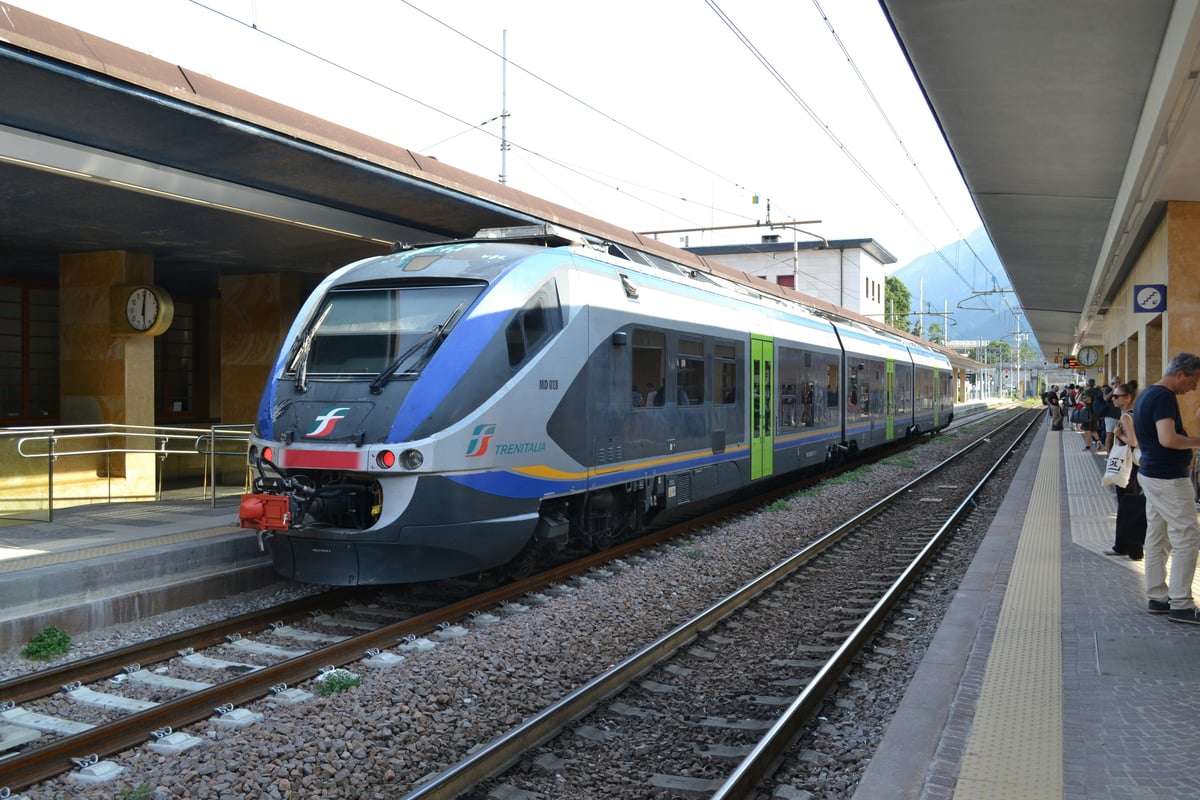 A red and white regional train waiting at a station platform under a metal canopy