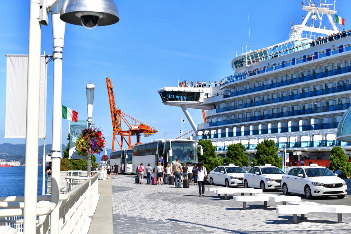 A shuttle bus parked at a cruise port beside a taxi rank, with ship superstructures behind