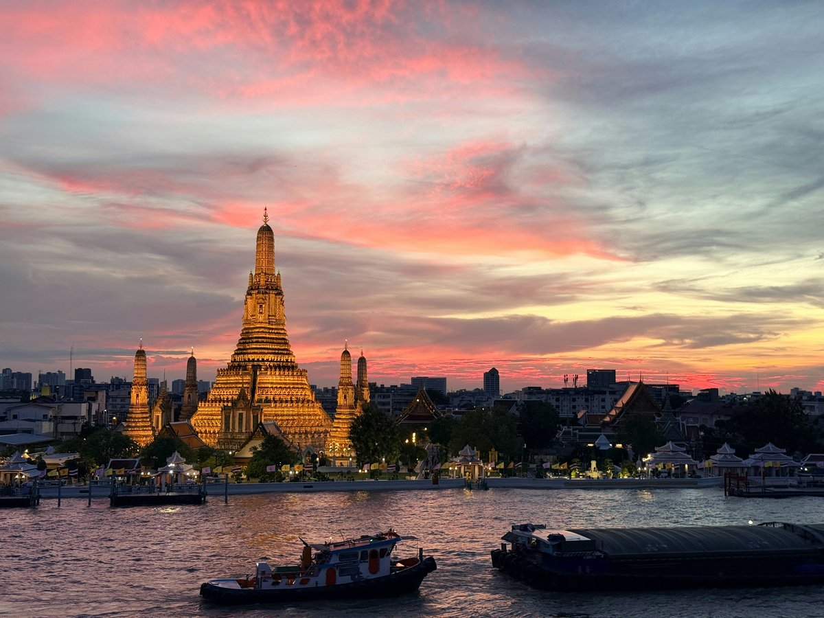 A wide establishing shot of Bangkok at dusk — temple spires against the modern skyline