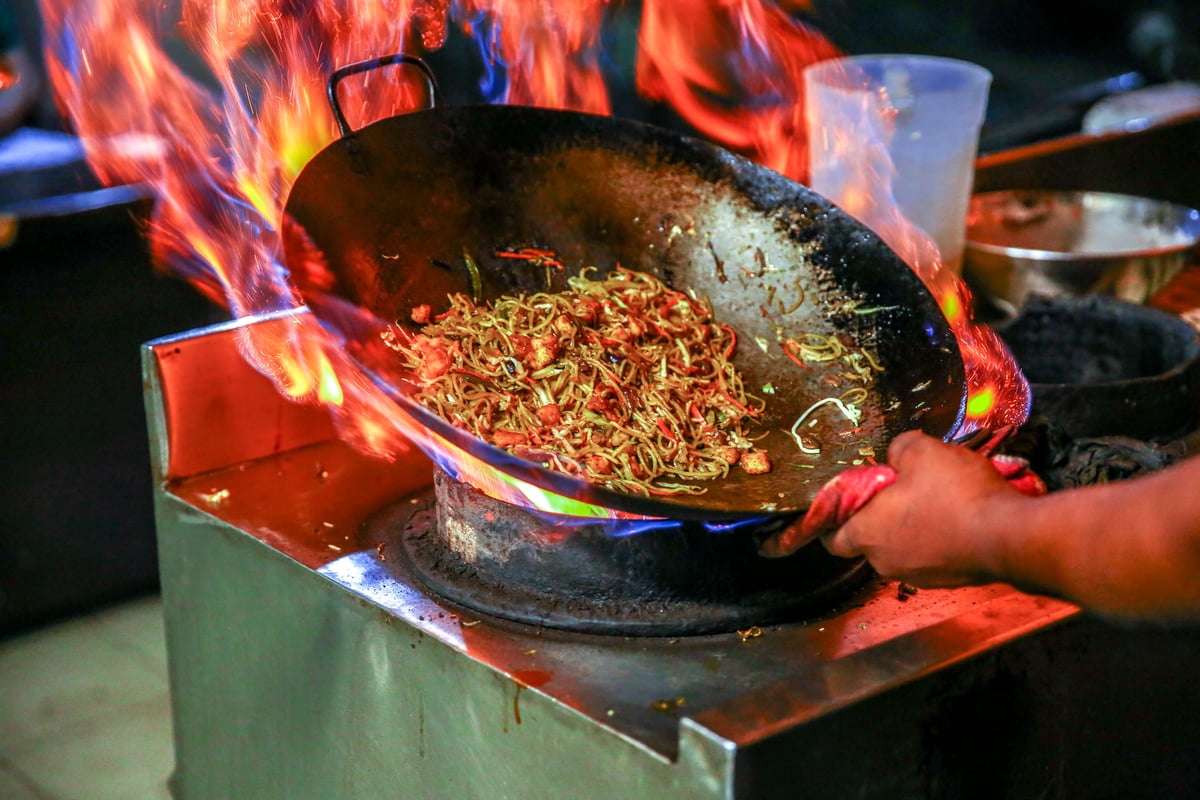 A Thai cooking class with woks, fresh ingredients, and students