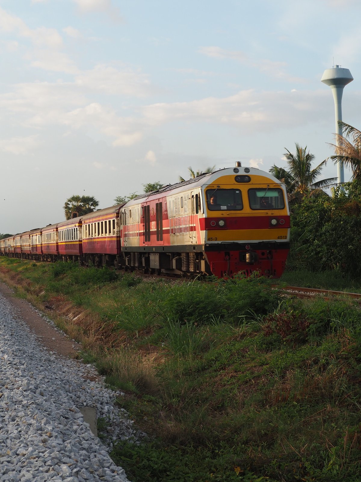 A Thai train traveling through green rice fields and hills