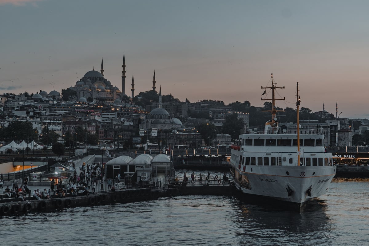A Bosphorus ferry on the water with the city skyline and a mosque silhouette behind