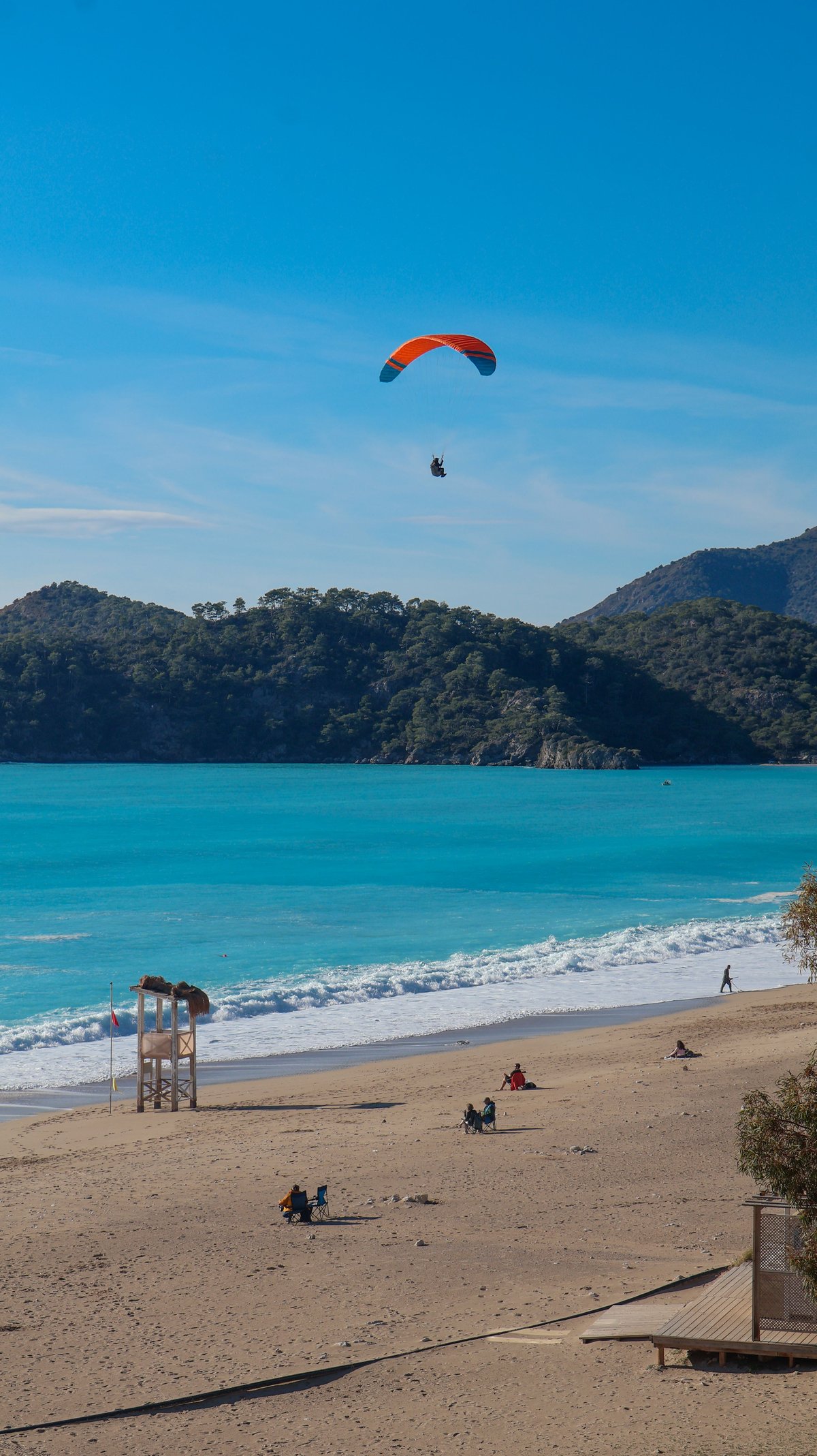 A tandem paraglider descending toward Ölüdeniz beach with the lagoon below