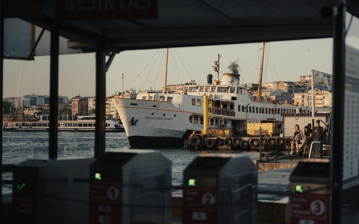 A white Istanbul commuter ferry moored beside the quay in daylight, seen through the card-tap turnstiles of the ferry terminal
