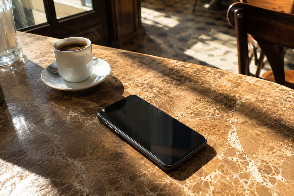 a phone on a table showing a blank screen beside a coffee cup, no visible apps or text, no faces