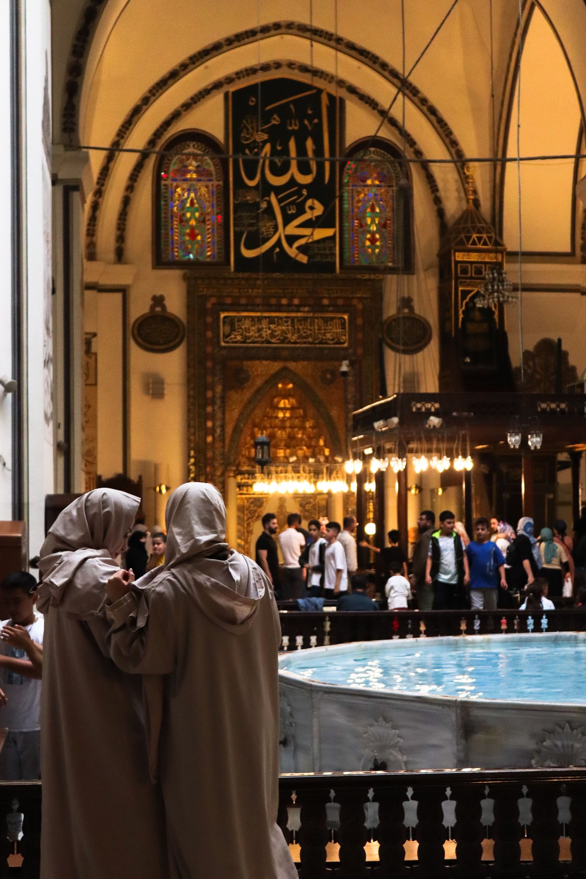 The interior of a grand Turkish mosque showing visitors dressed respectfully, no recognizable faces