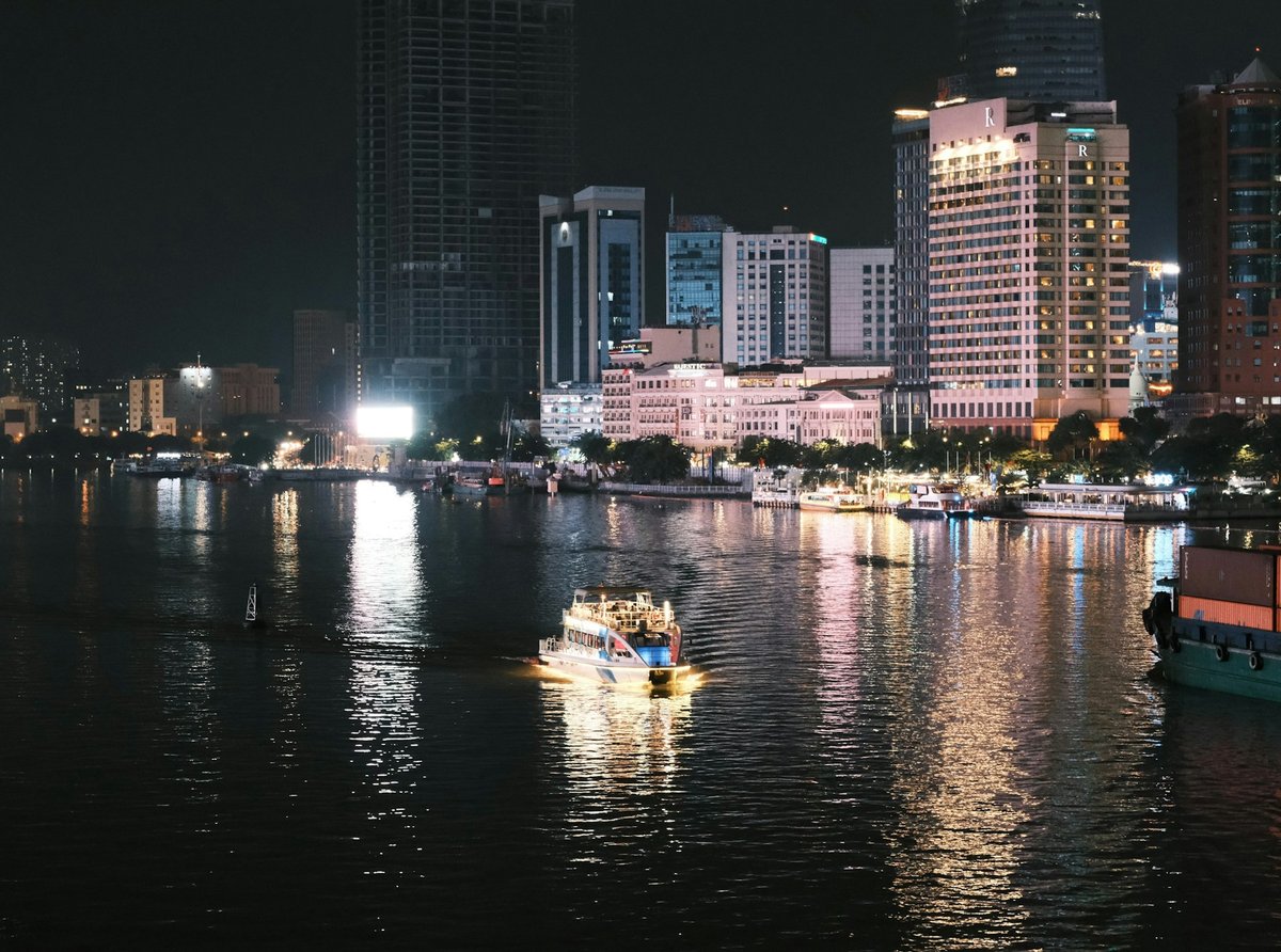 The Saigon River and the District 1 skyline lit at night, with a boat passing