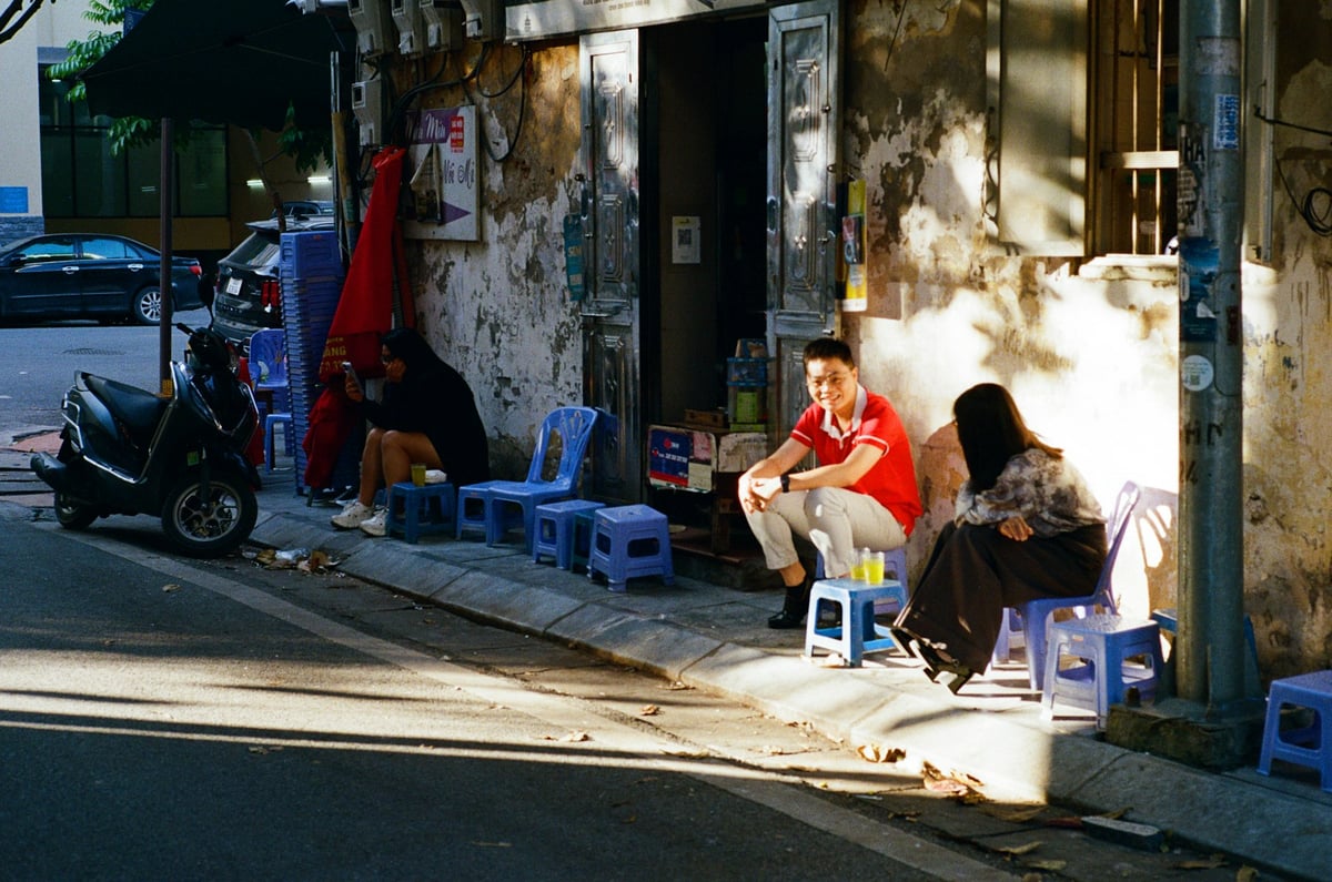 People sitting on low plastic stools outside a bar in a Hanoi alley