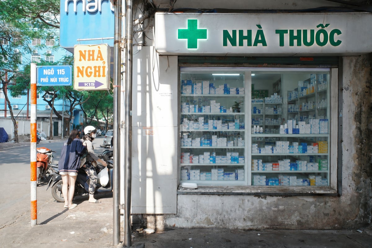 A Vietnamese pharmacy storefront with a green cross and a nhà thuốc sign above shelves of boxed medicines