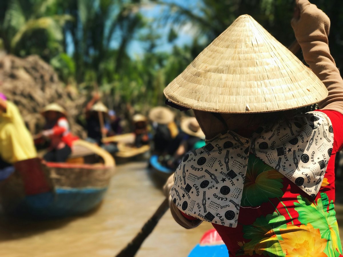 Boats crowded together at a floating market, a vendor in a conical hat in the foreground