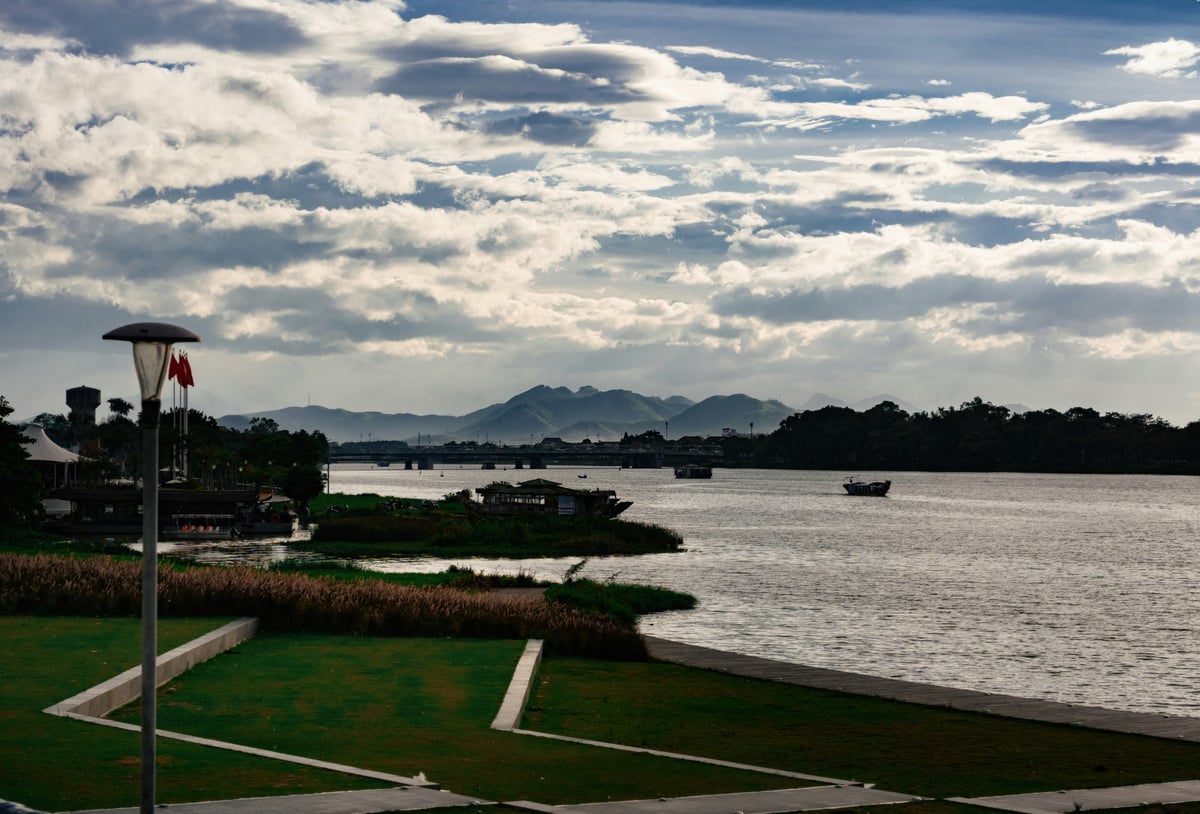 A wide river with small boats and low hills beyond, under a high cloudy sky