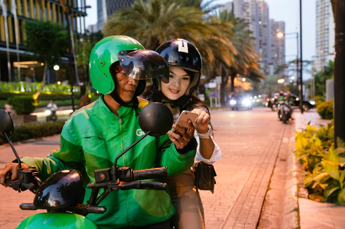 A ride-hailing motorbike driver carrying a passenger through evening traffic
