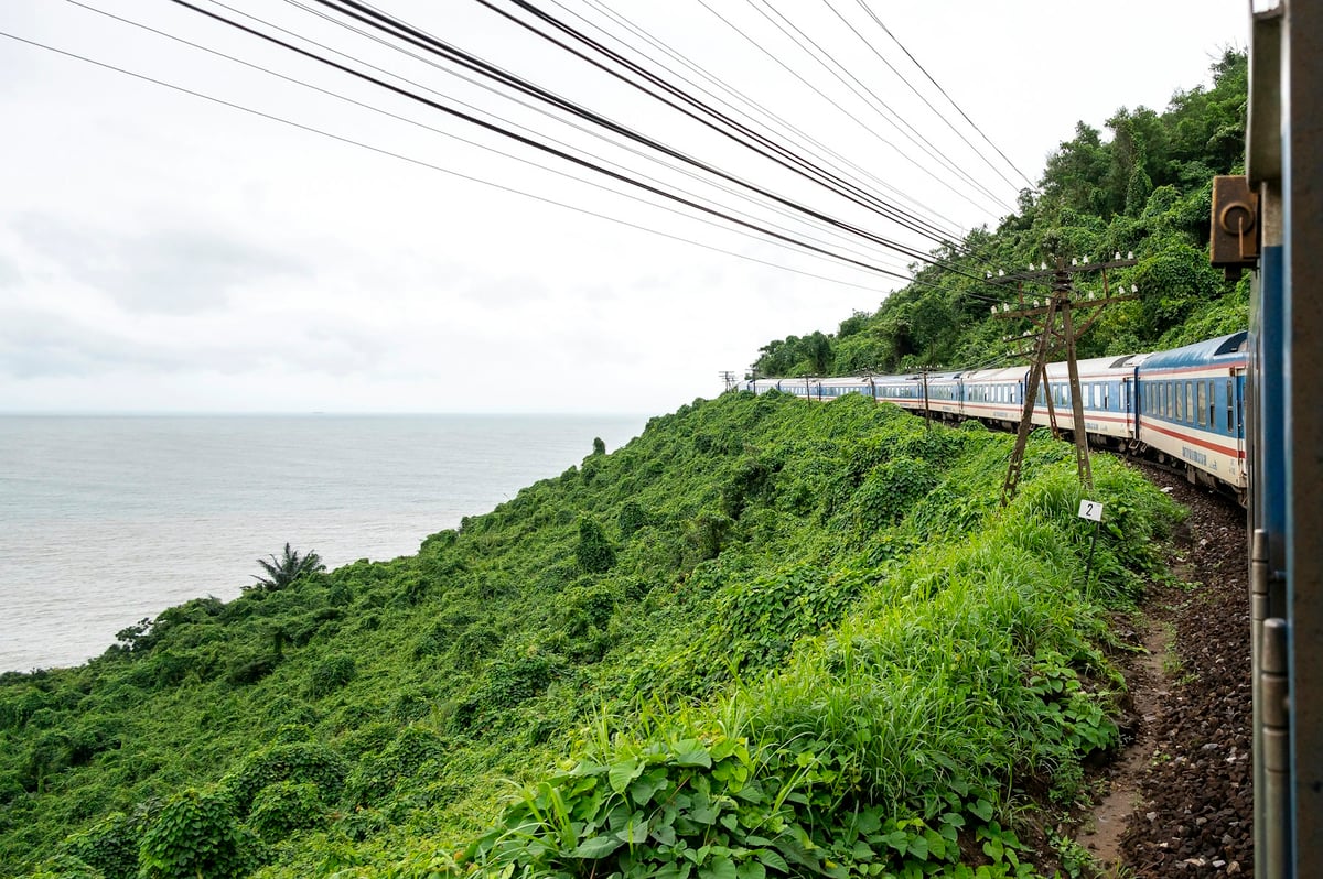 A train running along a green hillside above the sea on the central Vietnamese coast
