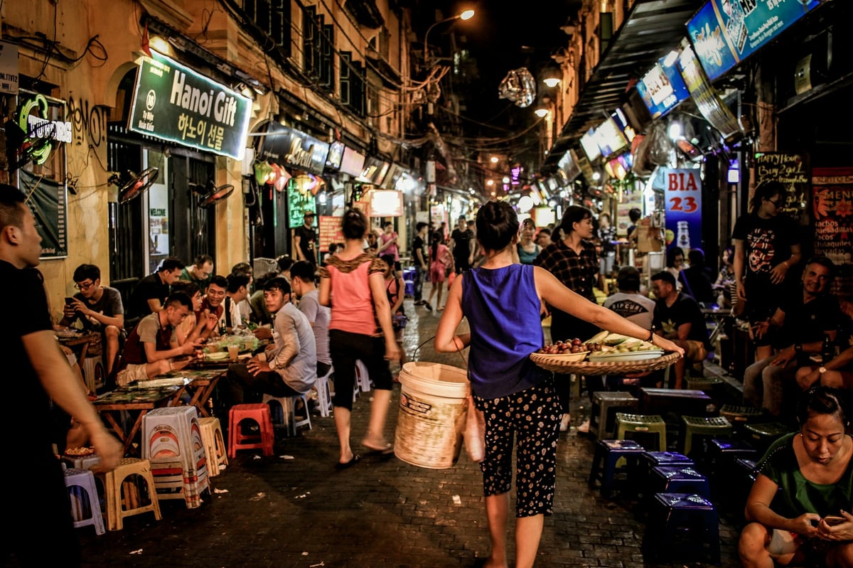 Diners on low plastic stools at a crowded Hanoi street-food corner at night