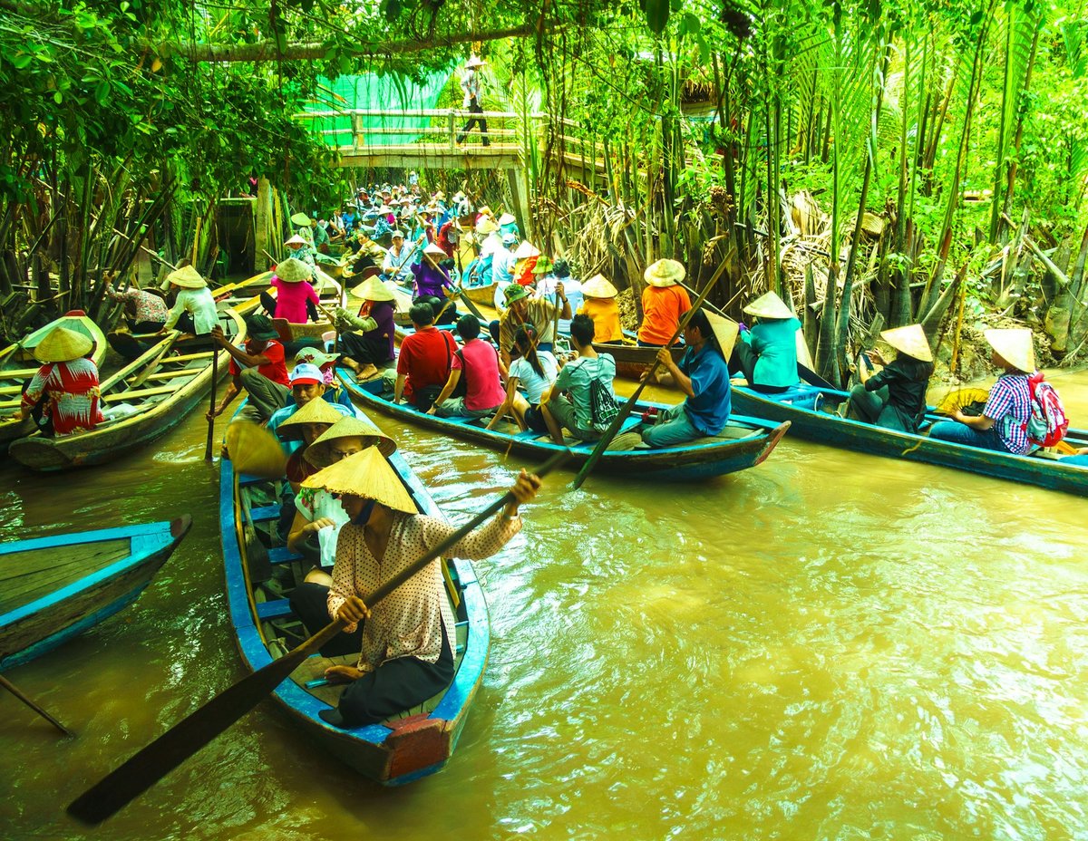 A crowd of visitor sampans packed into a narrow palm-lined canal in the delta
