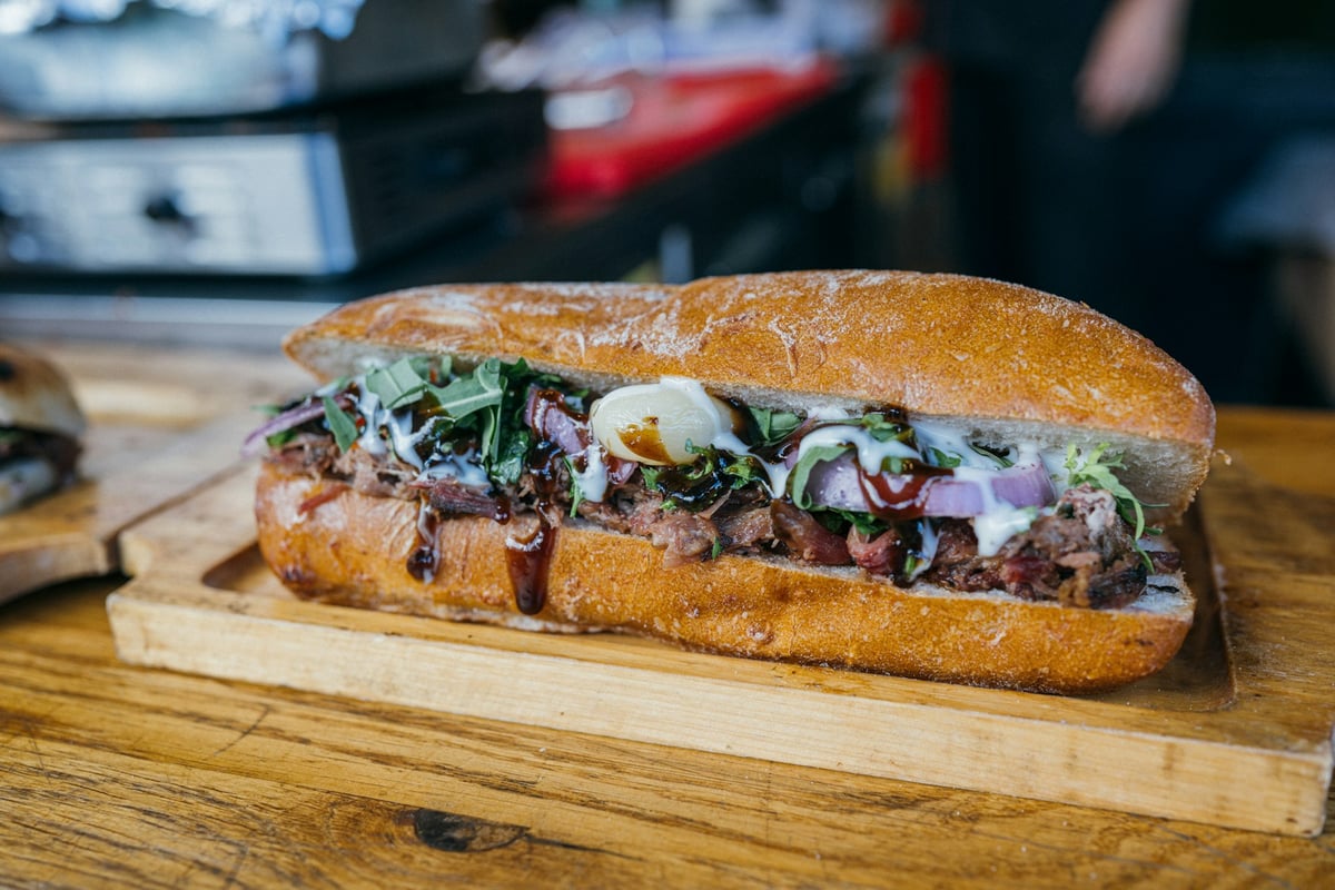 A banh mi split open on a board, filled with pork, pickles and herbs